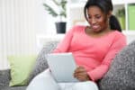 cheerful black woman using digital tablet in living room