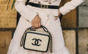 Woman holding designer quilted handbag with chain strap.